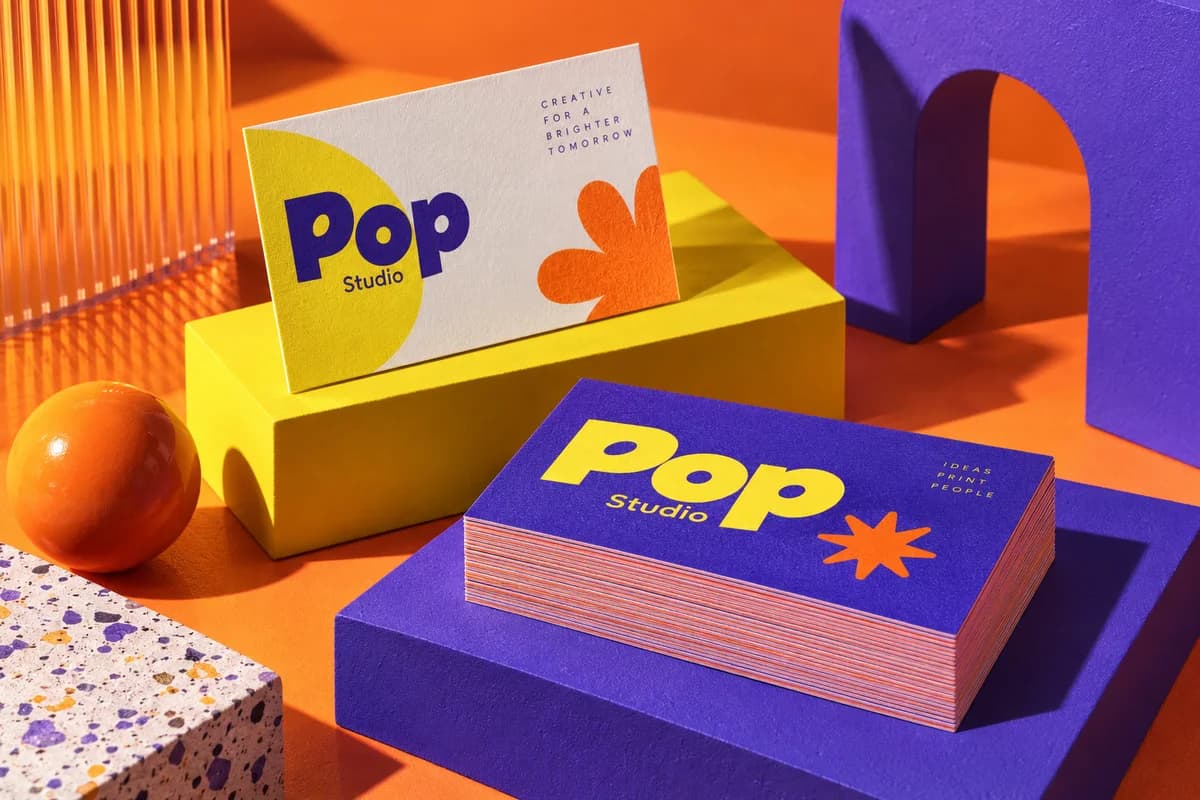 Two stacks of business cards with vivid fronts and backs and visible paper edges, with orange, electric violet, acid yellow artwork for a fictional creative design studio.