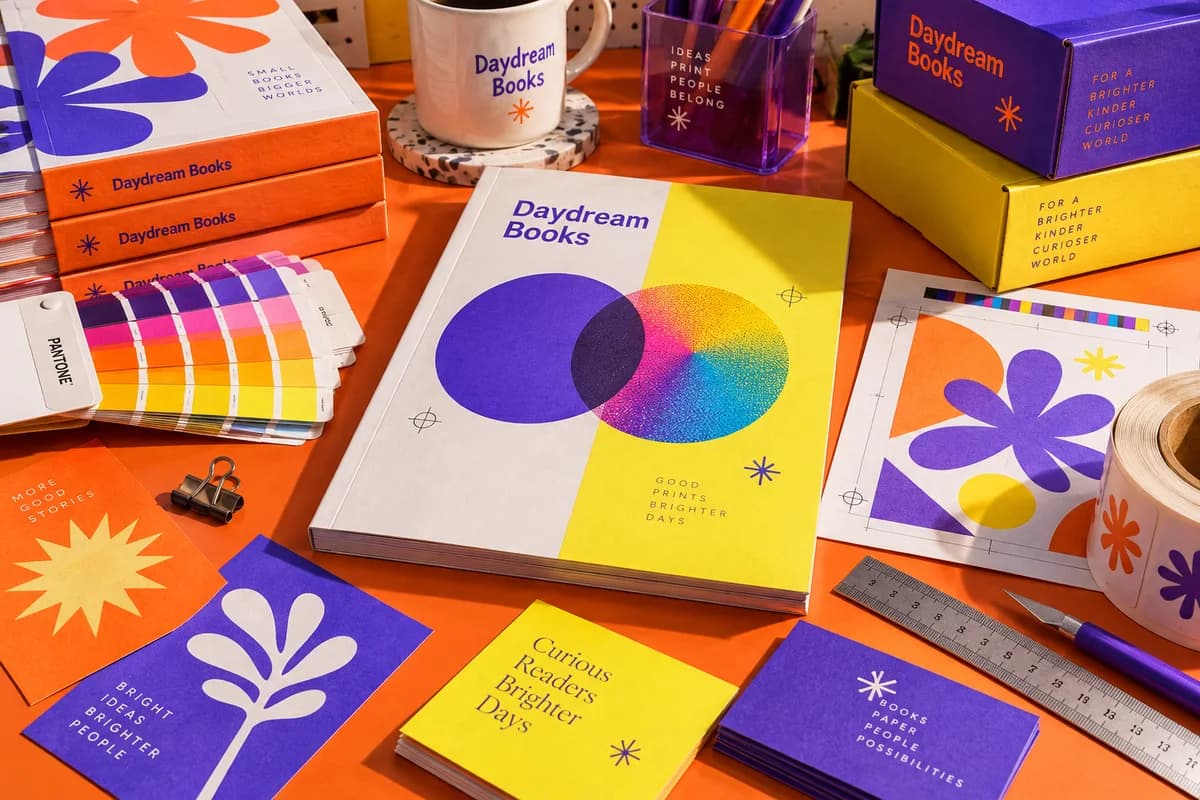 Colorful print proofs, paper swatches, a ruler and a clean designer workspace with prepared artwork, with orange, electric violet, acid yellow artwork for a fictional independent bookstore.